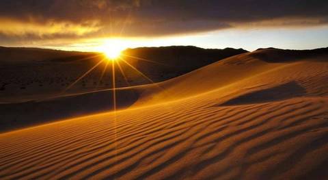 Sunrise over rippled desert dunes casting long shadows and a dramatic starburst