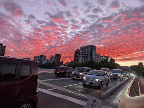 Evening traffic crossing a bridge beneath dramatic red-pink clouded sky over cityscape