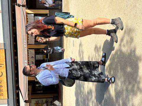 Two travelers enjoy ice cream outside a Japanese shop on a sunny day
