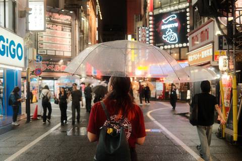 Night street scene in Japan with pedestrians and bright neon signs, subject holding clear umbrella in rain