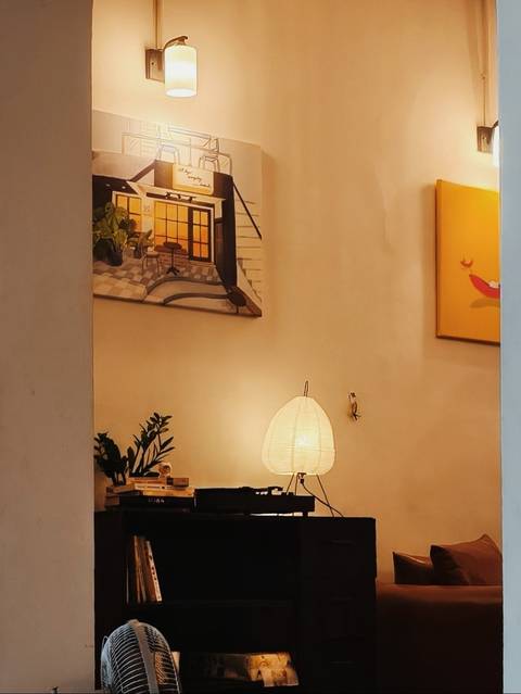 Cozy interior corner with a glowing table lamp, potted plants and wall art creating a warm ambiance.