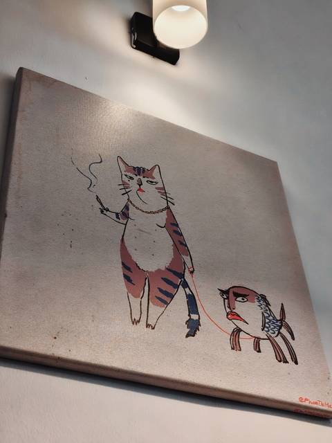 Close-up photograph of whimsical cat artwork smoking a cigarette on a wall canvas.