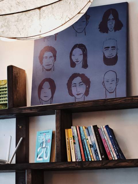 Art canvas displaying stylized portraits above a rustic wooden shelf of books.