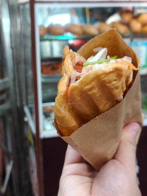 Hand holding a fresh Vietnamese banh mi sandwich wrapped in brown paper.