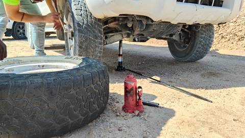 Mechanics changing a flat tyre on a 4x4 in a dusty desert setting.