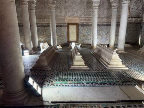 Ornate interior hall with marble tombs, mosaic walls and slender columns in soft light.