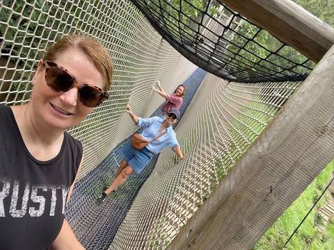 Three friends balancing on a high rope bridge and taking a selfie.