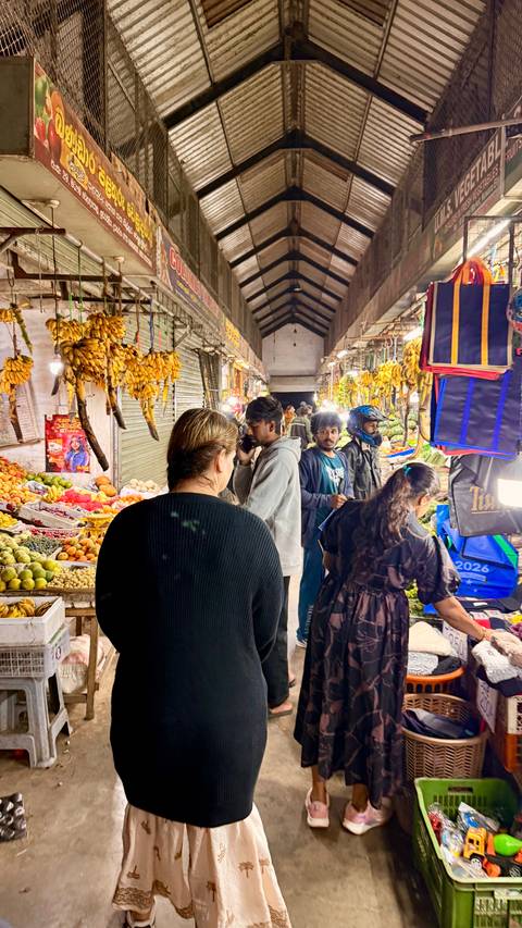 Busy indoor produce market with bunches of bananas and colourful fruit under bright lights.