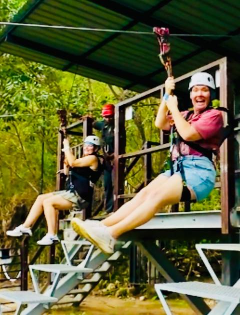Motion-blurred shot of two people zip-lining through trees.
