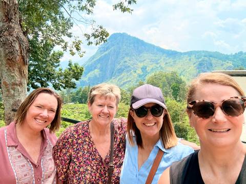Selfie of four women with sunglasses in front of a lush green mountain peak.