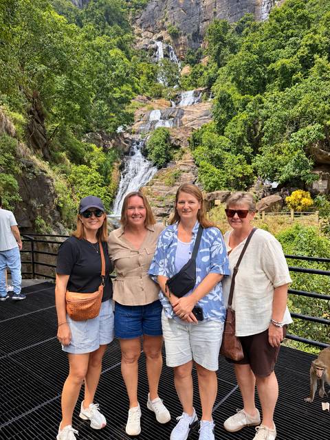 Travellers posing in front of a cascading waterfall surrounded by greenery.
