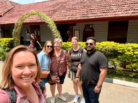 Small group smiling outside a colonial-style building with greenery.