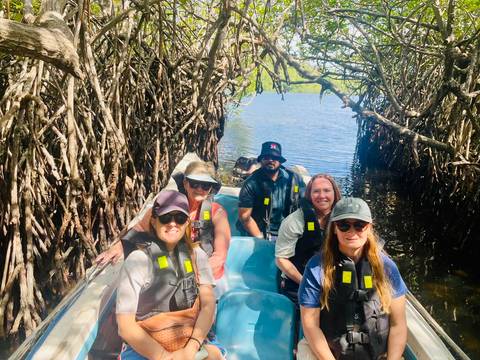 Small group wearing life vests in a boat navigating through mangrove tunnels.