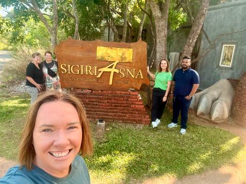 Selfie of travellers beside the wooden Sigiriya Asna resort sign.