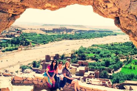 Three travelers sit beneath a natural stone arch overlooking the fortified village and lush valley of Ait Benhaddou.