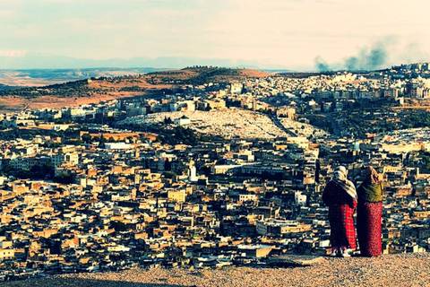 Two women in traditional dress overlooking the sprawling old cityscape of Fes from a high viewpoint.