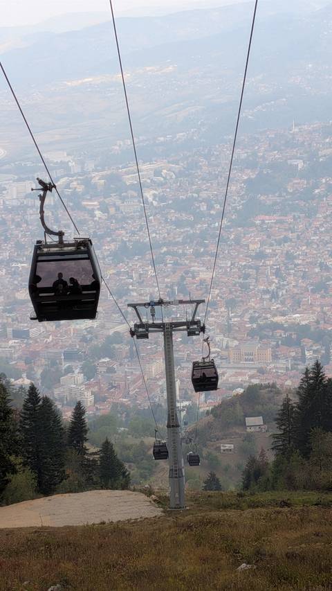 Cable cars ascending above Sarajevo with hazy cityscape spread out far below.