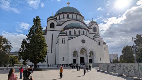 Grand Temple of Saint Sava with visitors gathered on the plaza under partly cloudy sky.