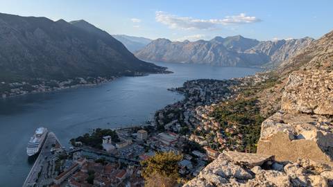 Sweeping view from mountain fortress over Kotor Bay with cruise ship and steep peaks all around.