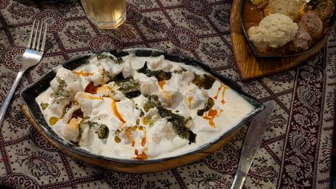 Traditional Bosnian dish in creamy sauce garnished with paprika oil served on patterned tablecloth.