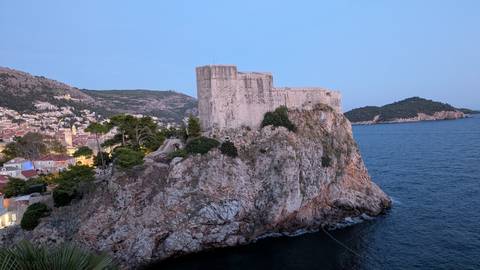 Fort Lovrijenac perched on a rocky cliff above the blue Adriatic with Dubrovnik rooftops nearby.