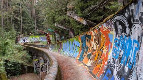 Abandoned Olympic bobsled track covered in vibrant graffiti winding through dense forest.