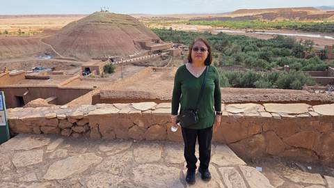 Traveler stands at viewpoint overlooking green oasis and desert hill topped with crosses near Ait Benhaddou.