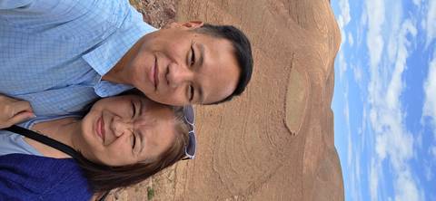 Selfie of couple with layered desert hills and rock formations forming patterns in the background.