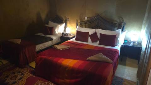 Twin and double beds with colorful covers inside a dimly lit desert tent room.