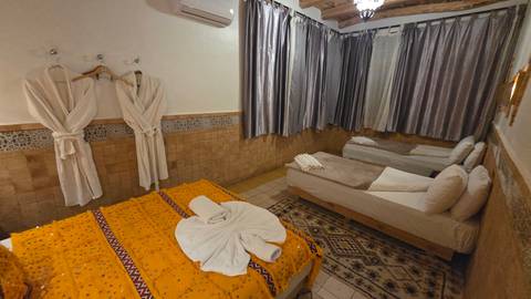Cozy Moroccan-style bedroom with orange patterned bedspread, twin beds, robes and tiled accents.
