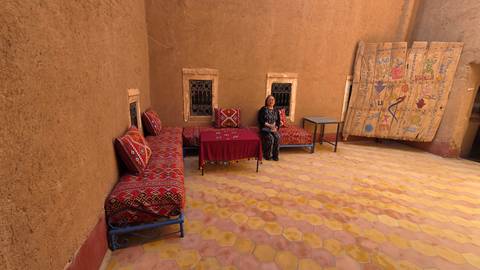 Open courtyard with patterned couches and a single guest seated at a red table against adobe walls.