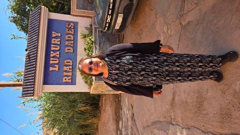 Traveller posing in front of sign reading 'Luxury Riad Dades' by a parked vehicle.