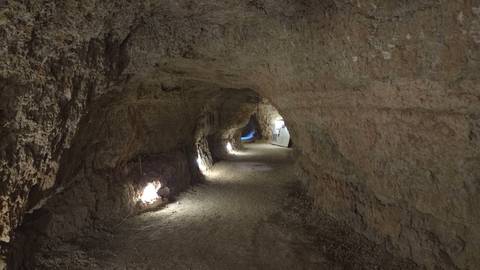 Dimly lit natural tunnel or cave corridor with rough rock walls and small ground lights.