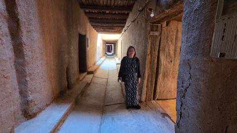 Traveller walking through narrow covered adobe passageway with wooden beams overhead.