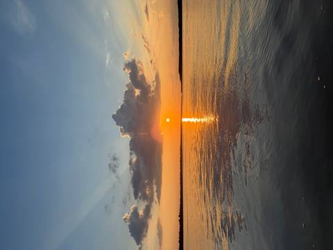 Vibrant sunset over calm Amazonian water with orange sun reflection and dramatic clouds.