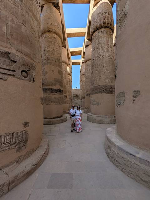 Couple stands among massive hieroglyph-covered sandstone columns beneath a slice of bright blue sky at an ancient temple.