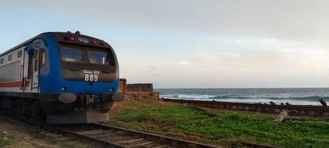 Blue coastal train carriage parked beside railway tracks that run right along the ocean shore