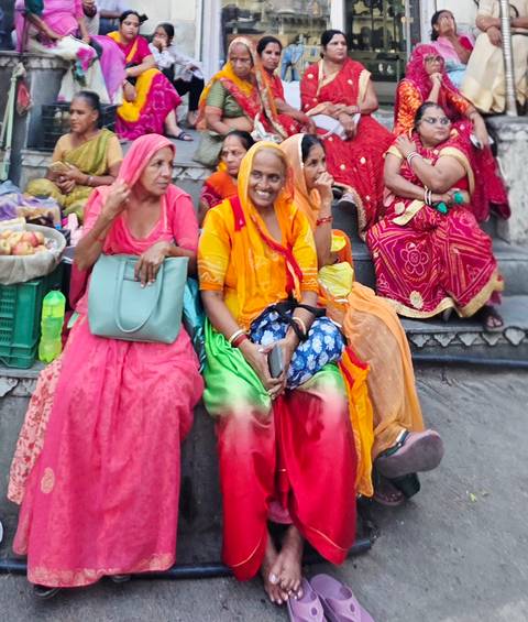 Women in vibrant Rajasthani dress resting on market steps with baskets of produce