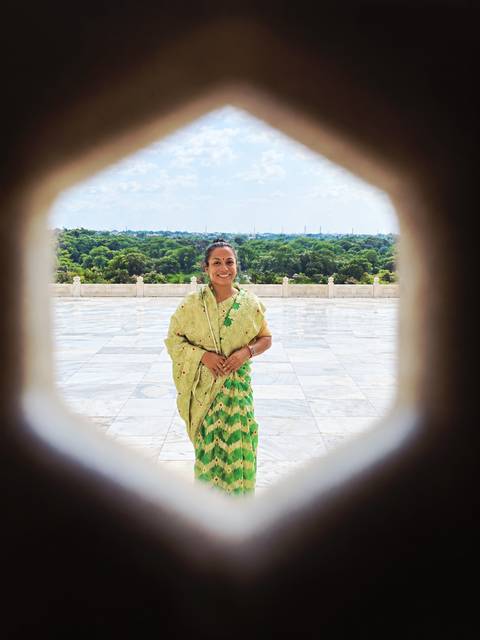 Smiling woman in sari framed through a circular marble opening with tree-filled courtyard behind