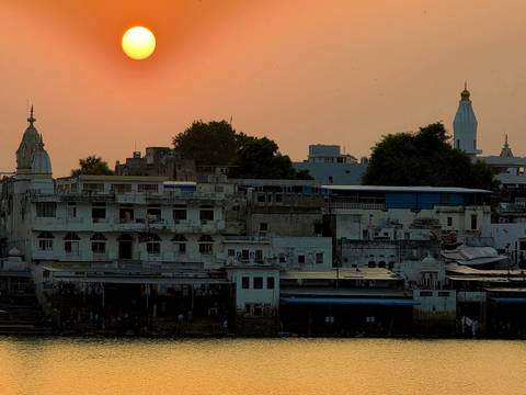 Orange sun setting over whitewashed buildings and temple spires of Pushkar
