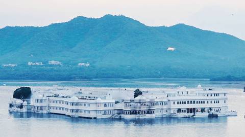 Iconic white Taj Lake Palace seemingly floating on Lake Pichola with blue hills beyond