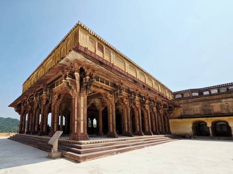 Intricately carved pillared hall of Amber Fort glowing in warm sunlight