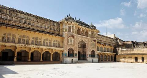 Sunny courtyard of Amber Fort featuring ornate archways and patterned windows