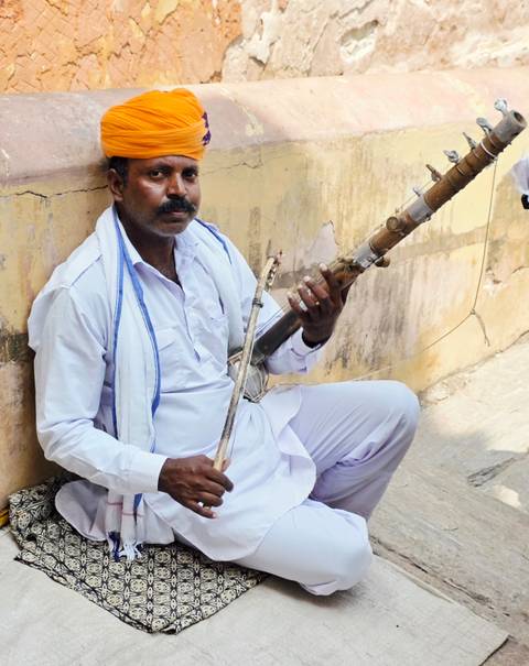 Traditional Rajasthani musician seated against a wall playing a rustic string instrument