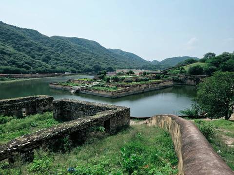 Rectangular garden island surrounded by calm water and forested hills at a historic fort lake.