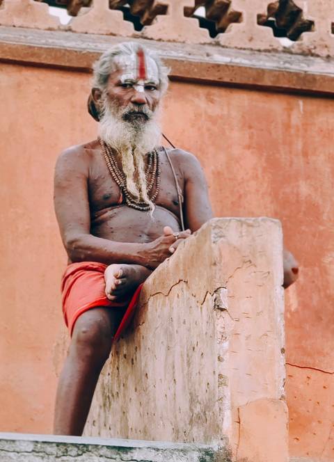 Close-up of a seated sadhu wearing prayer beads against an earthy terracotta wall.
