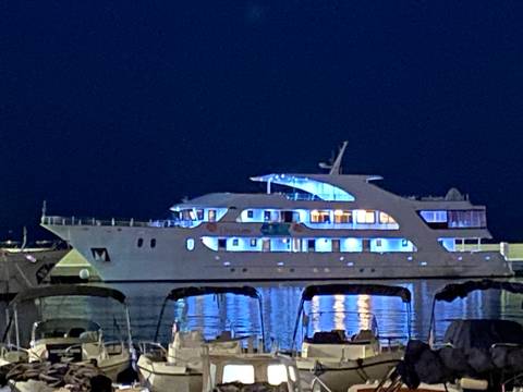 Illuminated white cruise yacht moored in a harbor at night with reflections on water.