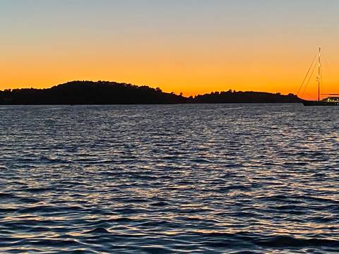 Golden sunset over calm sea with silhouette of low island and distant sailboat.