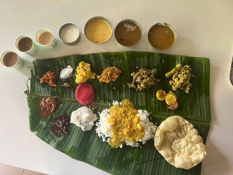 Traditional South Indian banana-leaf meal with assorted curries, rice and tea cups.