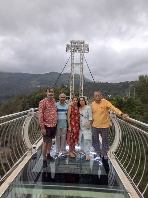 Family group posing on a metal suspension glass bridge with misty hills behind.